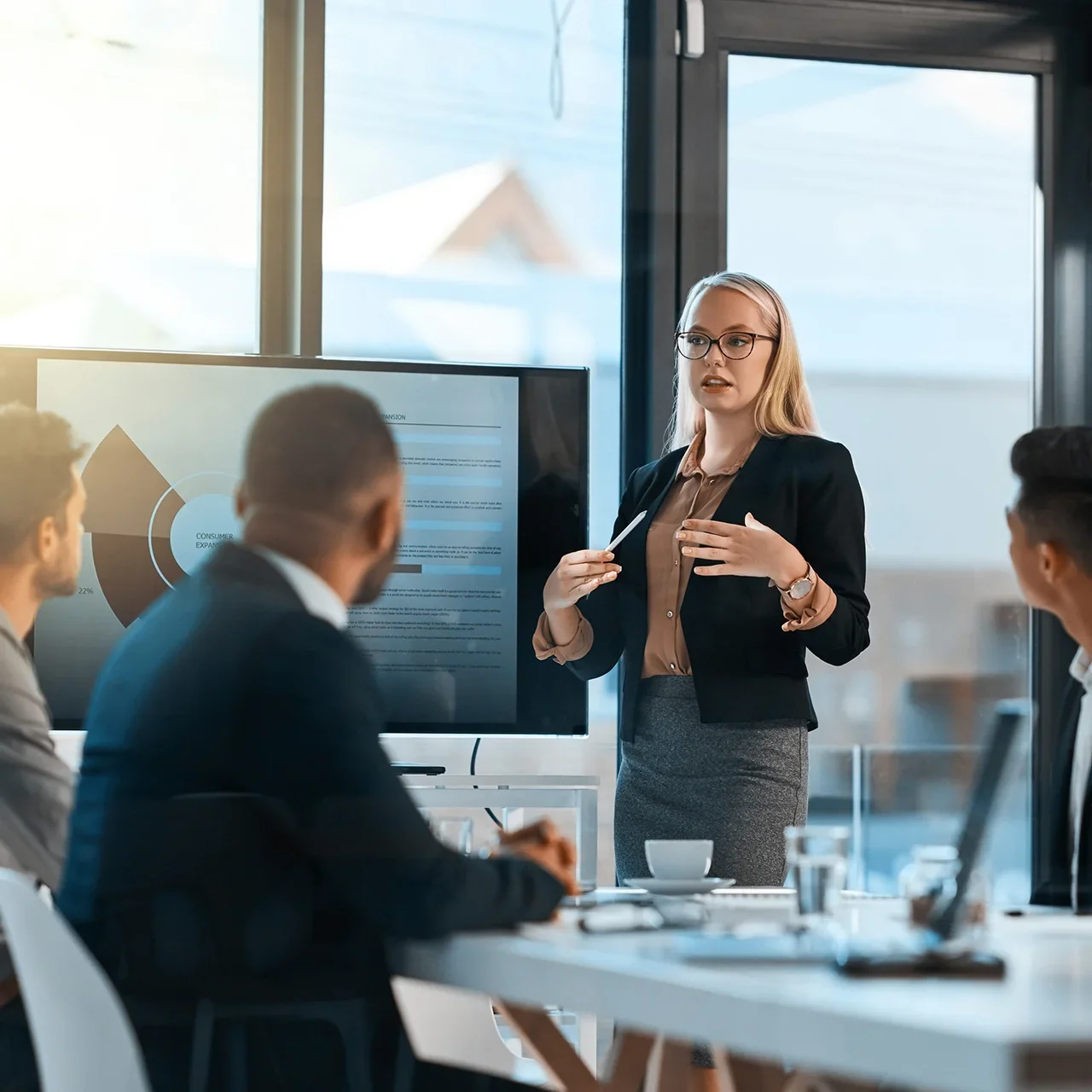 A woman presents in front of a monitor in a meeting with three others.