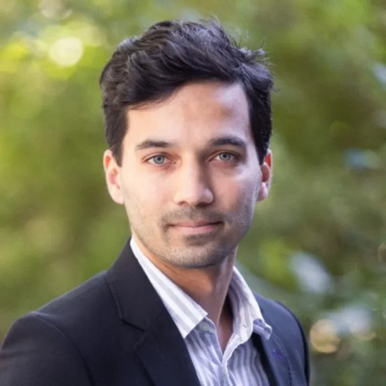 A professional portrait of Liam Weber against a neutral, blurred gray background.