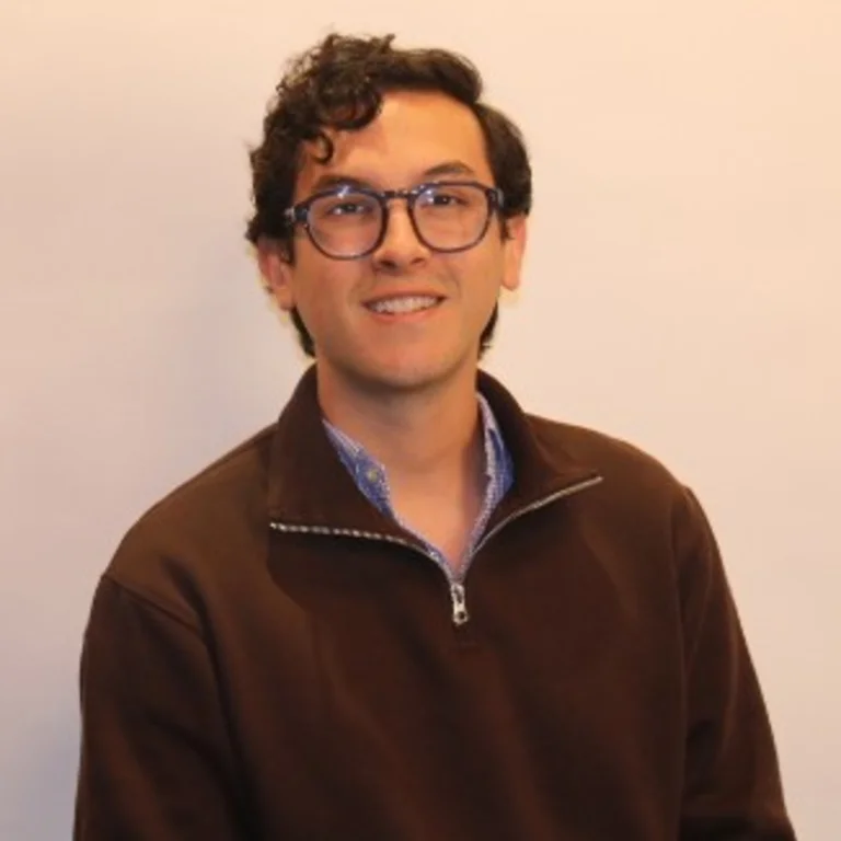 professional headshot of Nico Gallego wearing glasses, black quarter zip sweater and blue shirt
