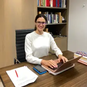 A photo of Helena Economides, '20SPS, Nonprofit Management, sitting at a desk with a laptop.
