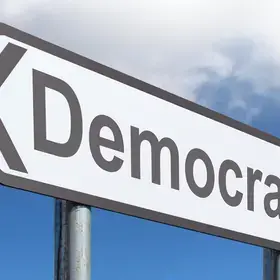 White road sign displaying the word "democracy" in black lettering