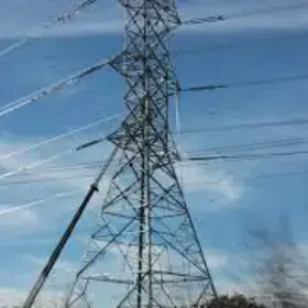 An electricity transmission tower stands at the center of the photo. The photo of the tower was taken from the ground and during the day
