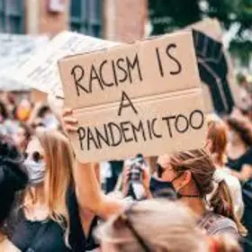 protestor holds a sign saying "racism is a pandemic too" at a black lives matter rally
