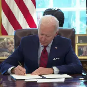 President Biden signing document while sitting at desk in Oval Office