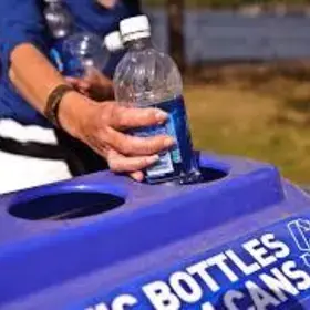 arm placing plastic bottle in a blue recycling bin