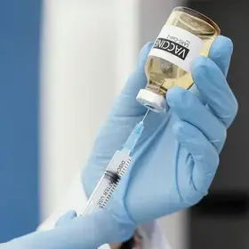 gloved hand inserting a syringe into a vaccine vial