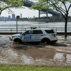 An NYPD car drives through a flooded street.