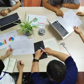 Overhead view of a group meeting with visible notes, charts, computers, and use of data.