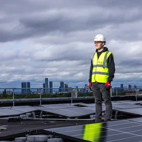 Solar panel worker standing on rooftop amid solar array with city in the background