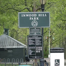 Inwood Hill Park NYC Parks Department sign with visitors shelter and trees in the background