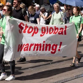 People march in a climate protest, holding a banner that reads "Stop global warming!"