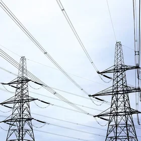 Two tall metal power line pylons supporting multiple high-voltage electrical cables against a cloudy sky.