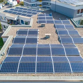 Aerial view of a flat-roofed residential building covered with multiple rows of solar panels.