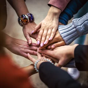 9 hands stacked on top of each other in a circle, in a display of teamwork