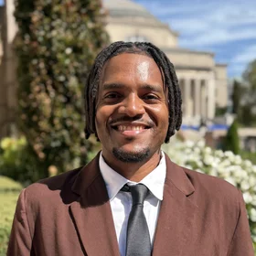 professional headshot of Xavier brown suit and black tie 