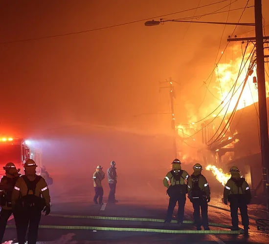 Firefighters near a burning home in the Palisades neighborhood in Los Angeles, California