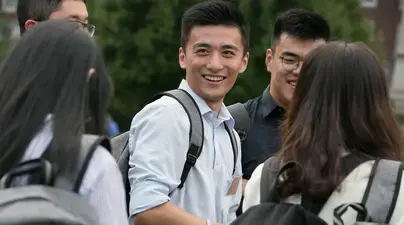 Students on campus wearing backpacks and smiling.