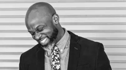 Black and white image of Black man in suit blushing and smiling with his eyes closed