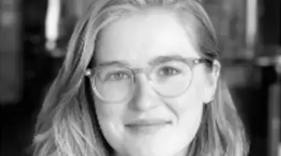 Black and white headshot of youthful blonde womand smiling with frosted round framed glasses