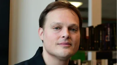 Caucasian man smiling closed mouth in front of a stack of books