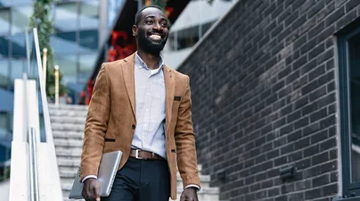A man descends an outdoor staircase in the city with a laptop under his arm.