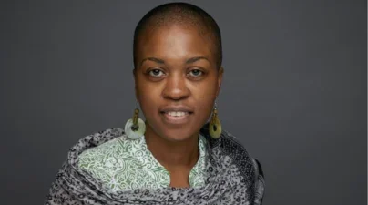 woman of color against gray backdrop smiling in green white and gray patterned shirt and scarf