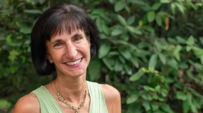 smiling woman with dark bob in front of wall of foliage