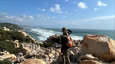 A student stands among rocky coastal outcrops overlooking the ocean.